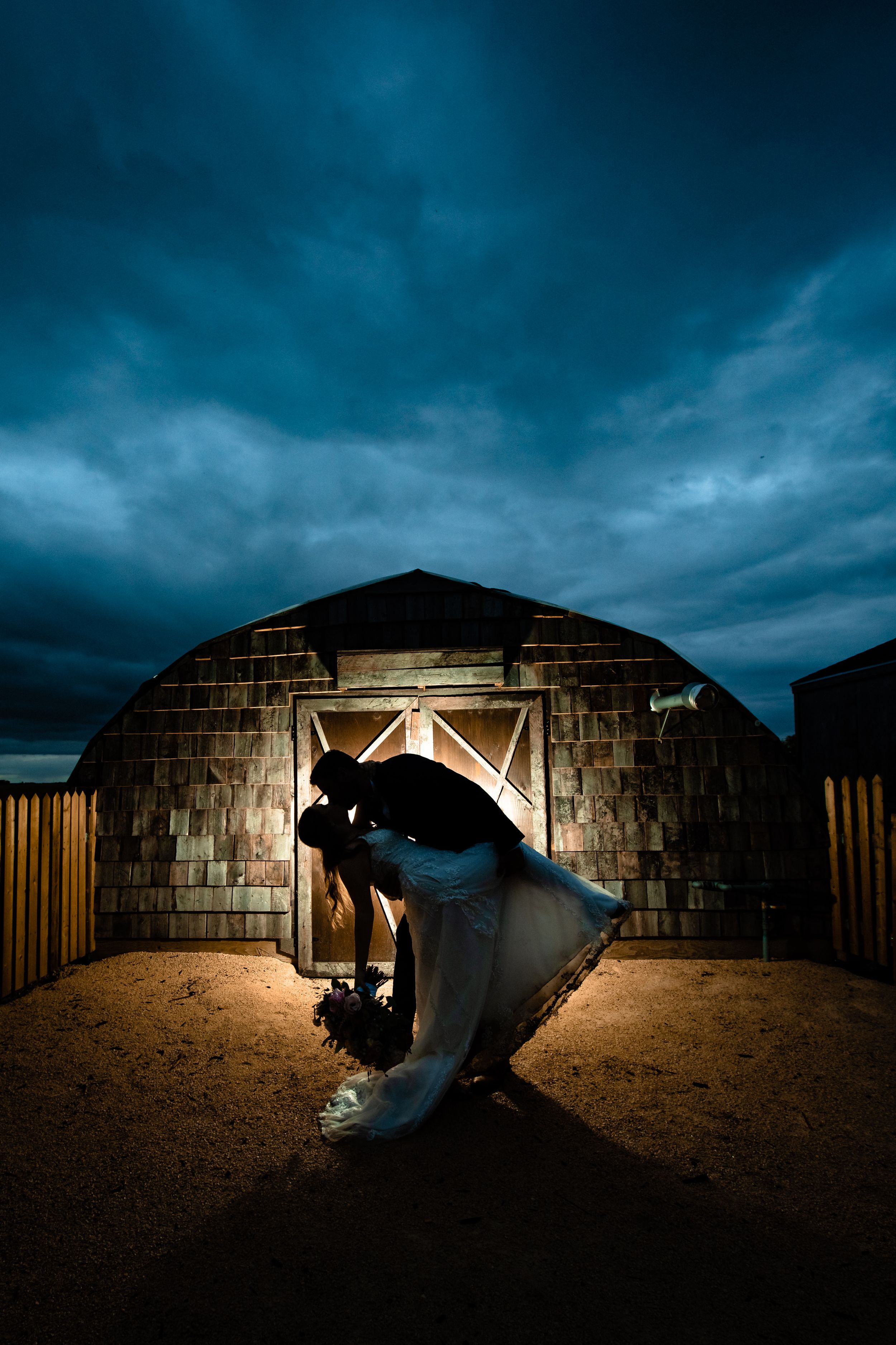 Silhouetted figure in a dramatic pose against illuminated stone building entrance under moody dark blue storm clouds.