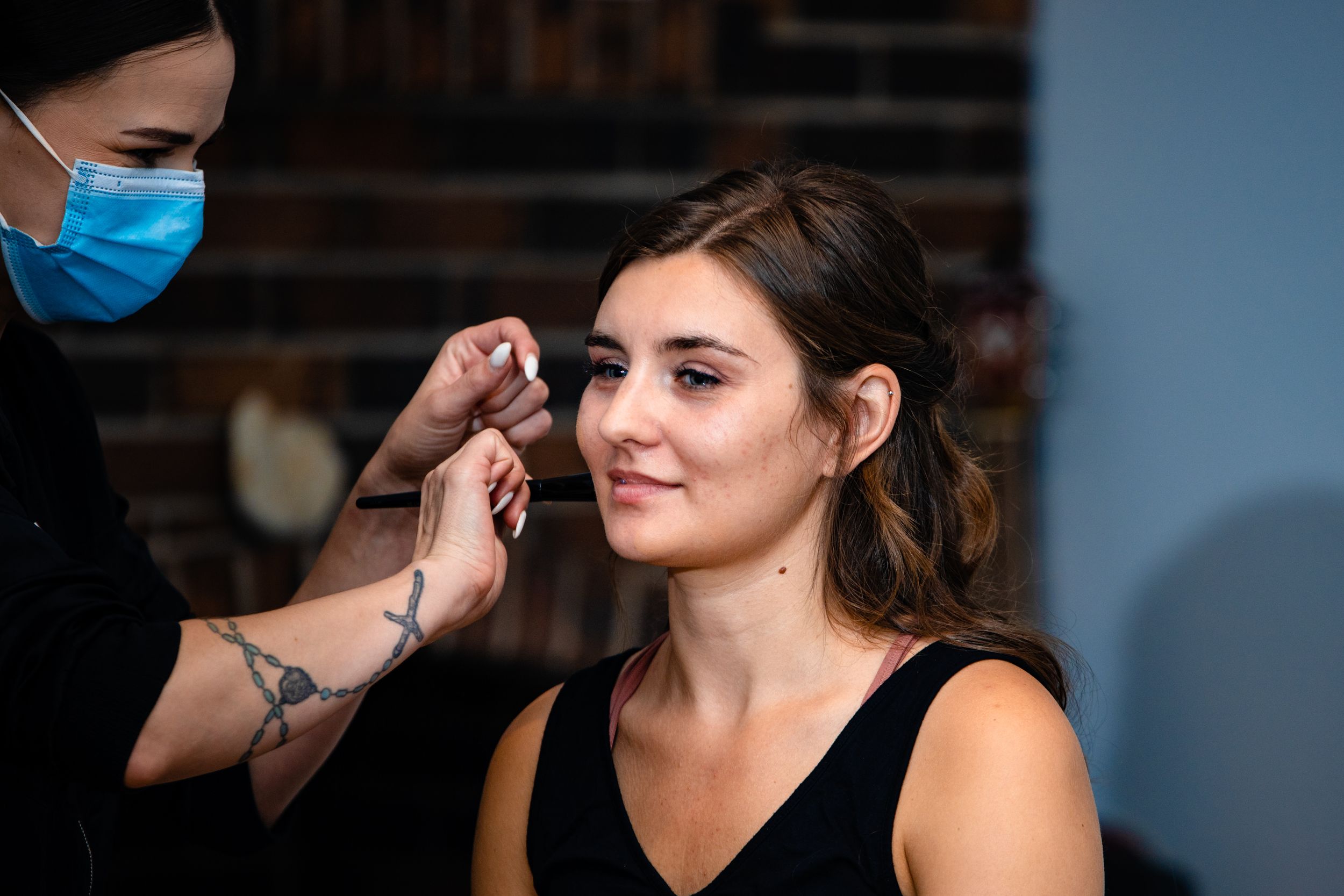 A makeup artist wearing a blue mask applies cosmetics during a beauty preparation session.