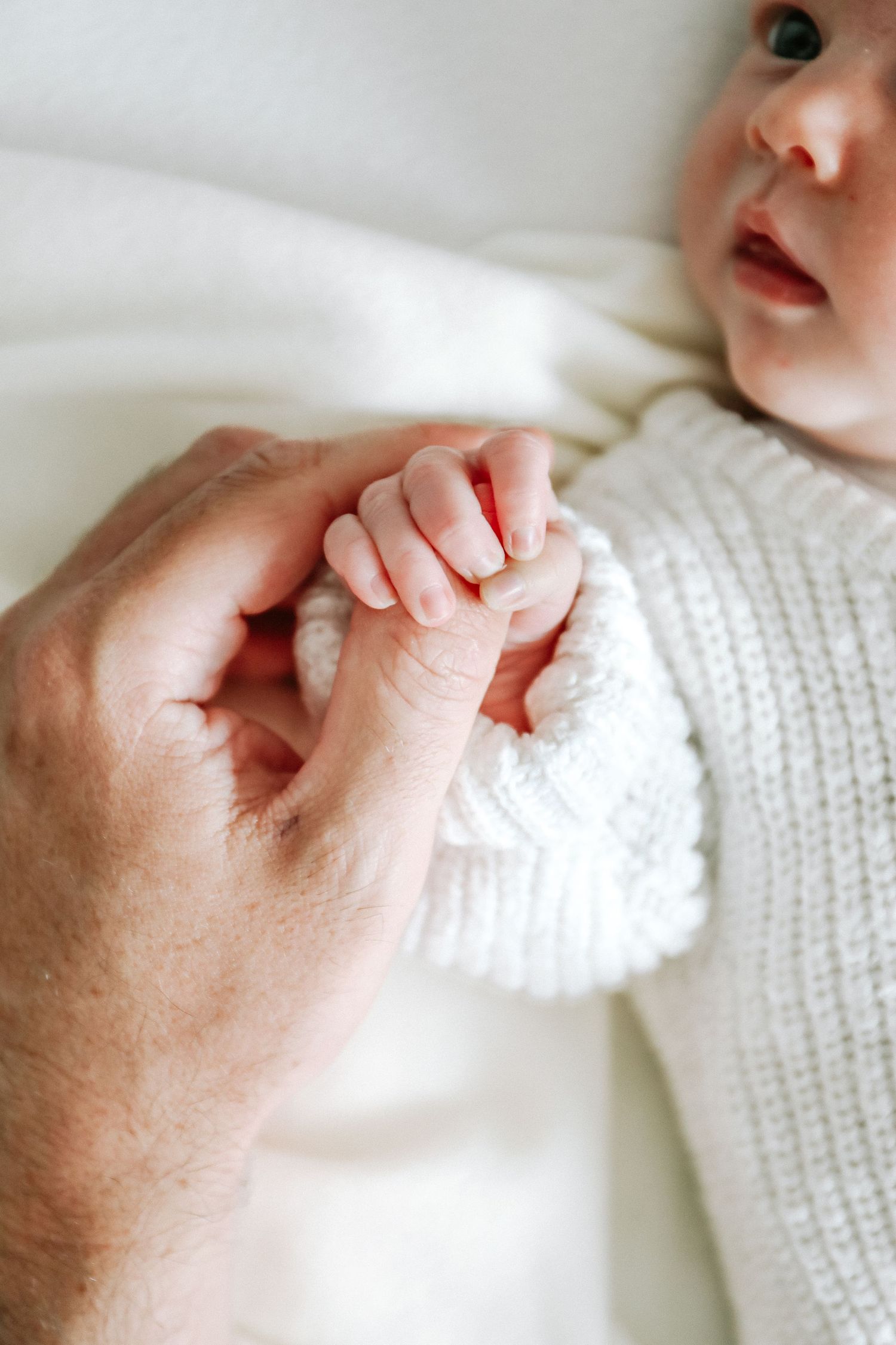 A small baby hand gently grasps an adult's finger while wearing a cozy white knit romper, during newborn photoshoot in Nottingham