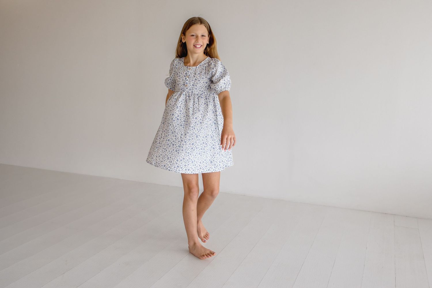 Child wearing floral print dress twirling and playing in bright white studio space.