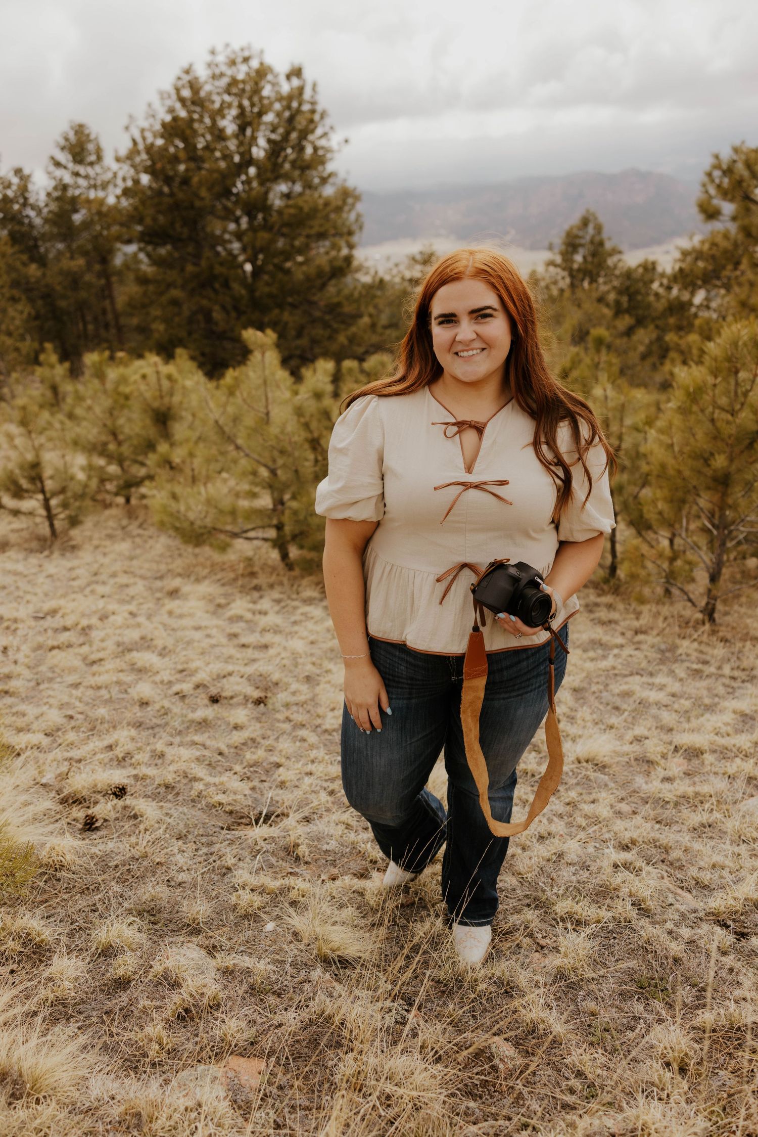 Photographer in casual attire crouching in desert landscape with mountain views.