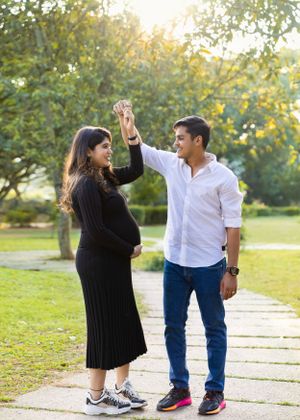 Outdoor maternity photo of couple dancing together on stone path during golden hour.
