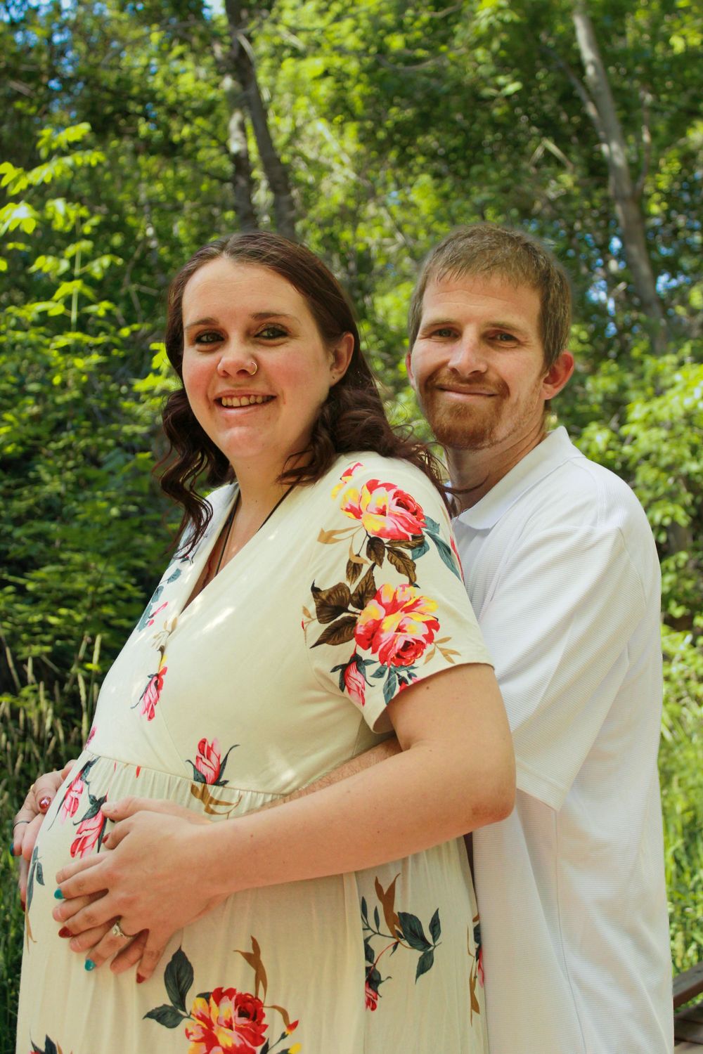 Maternity photoshoot featuring couple in natural outdoor setting with floral dress and white shirt.