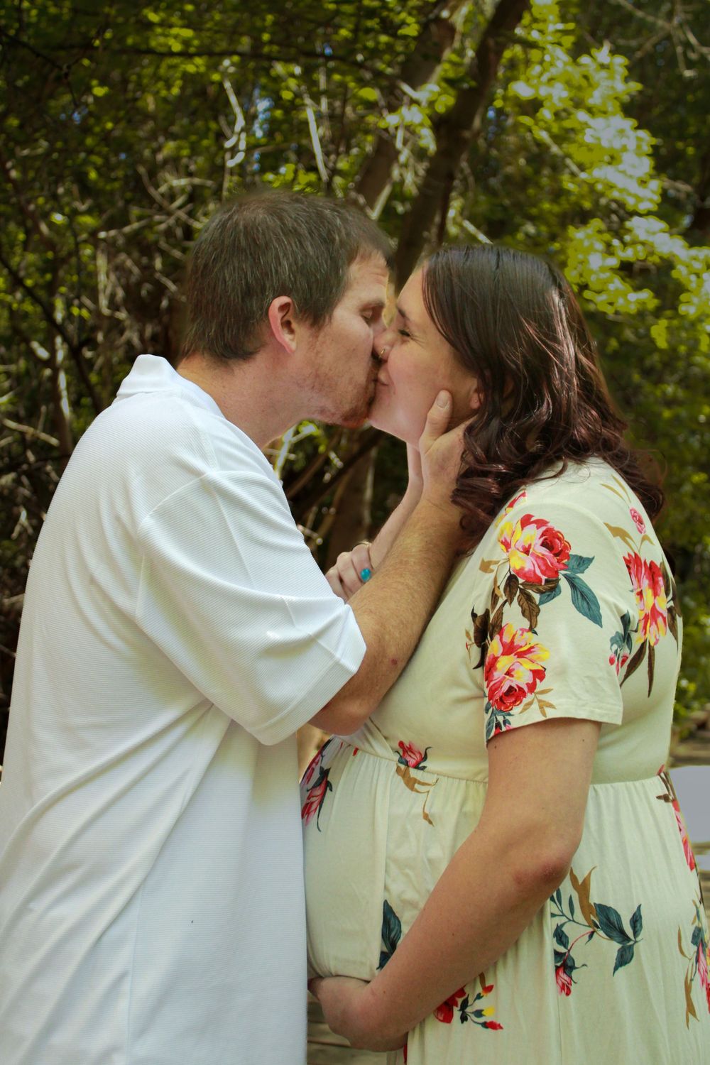 A couple shares an intimate moment outdoors, with the woman wearing a floral dress.