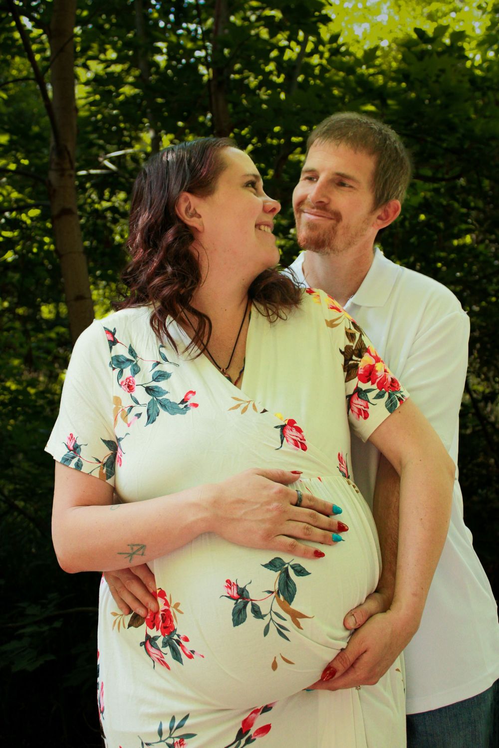 A romantic outdoor maternity photoshoot featuring a couple in white and floral attire.