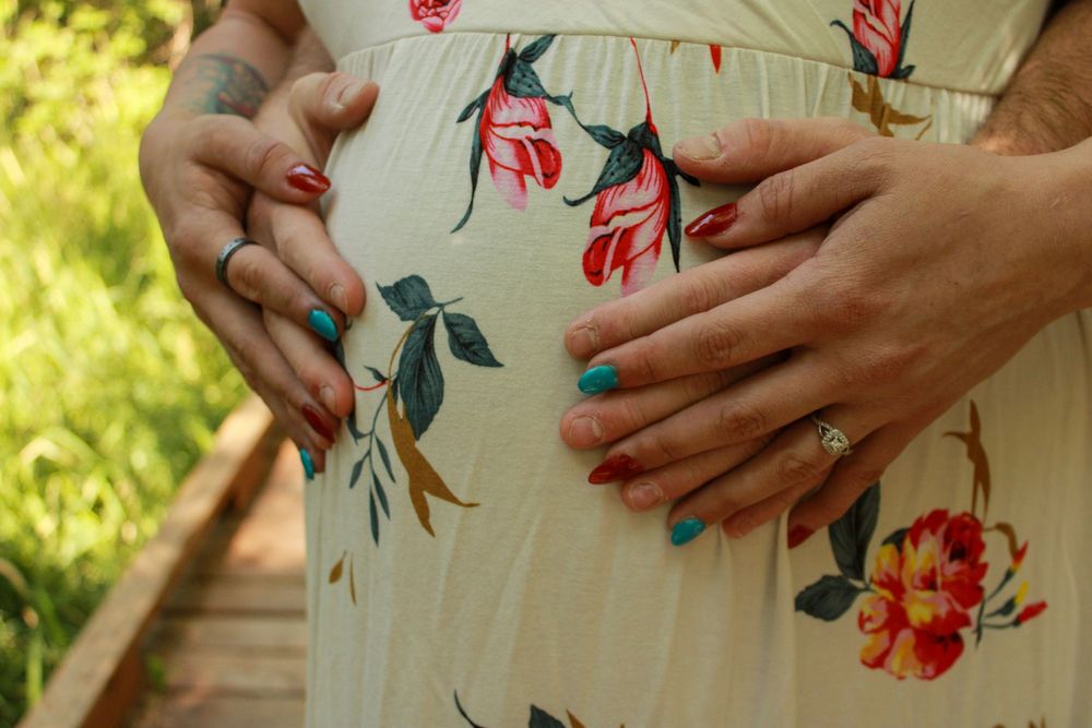 Close-up of engagement ring on hand wearing floral dress against green garden background.