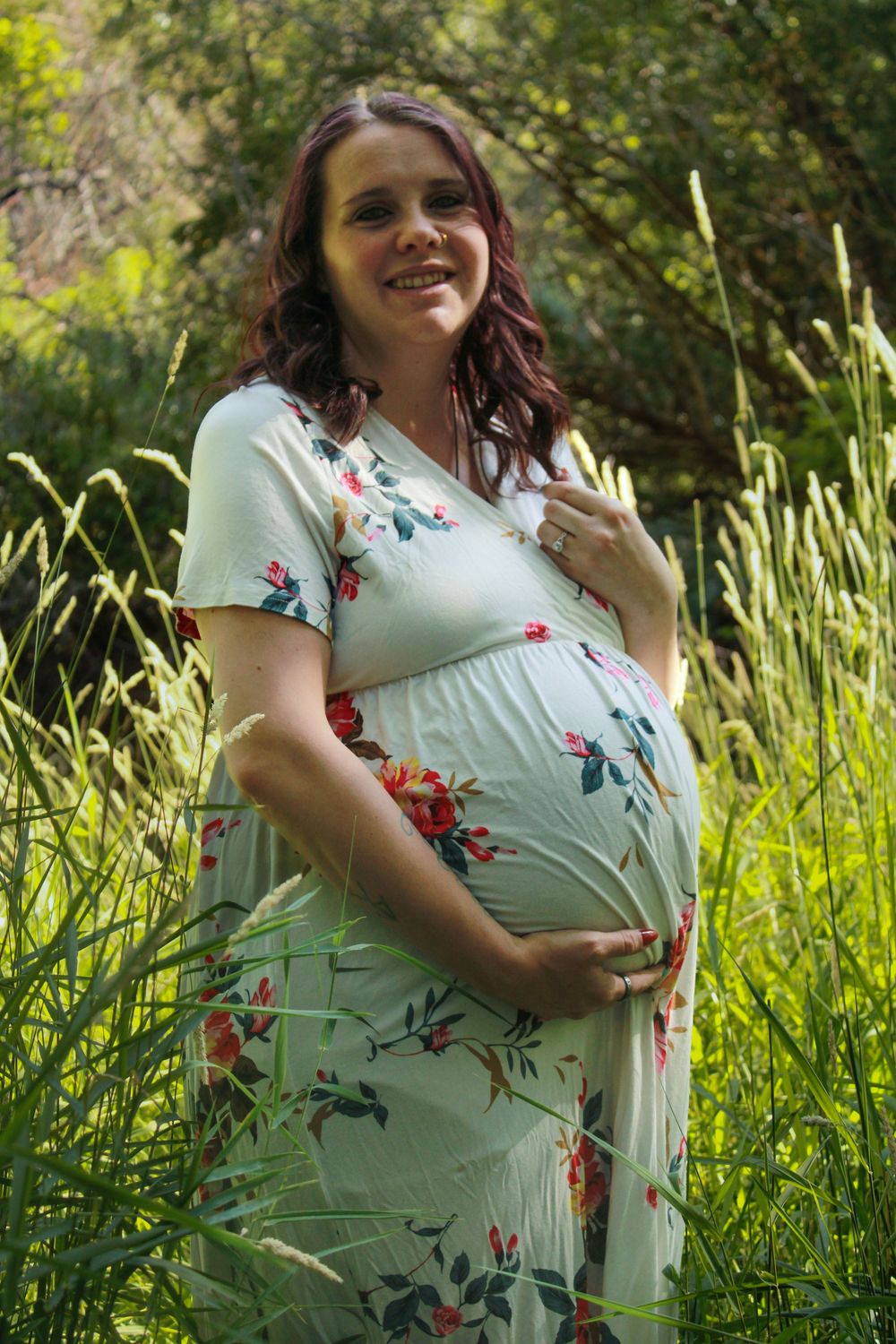 A pregnancy portrait session in tall grass with a white floral dress against a nature backdrop.