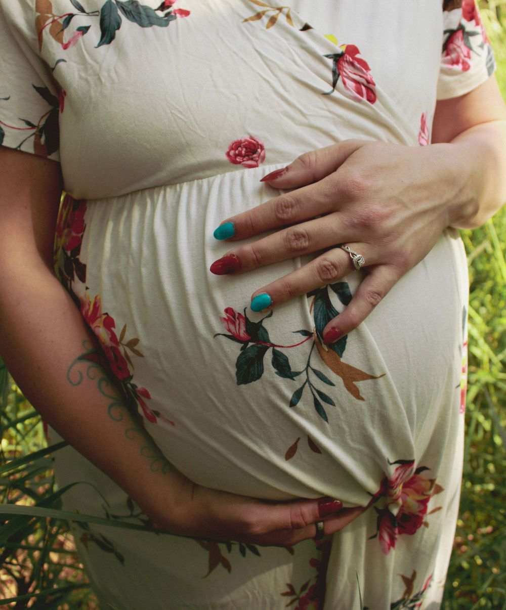 Close-up shot of hands cradling a pregnant belly in a white floral dress.