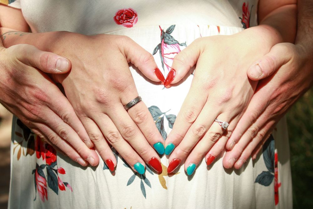 Hands forming heart shape over pregnant belly with butterflies and floral decorative overlay design.