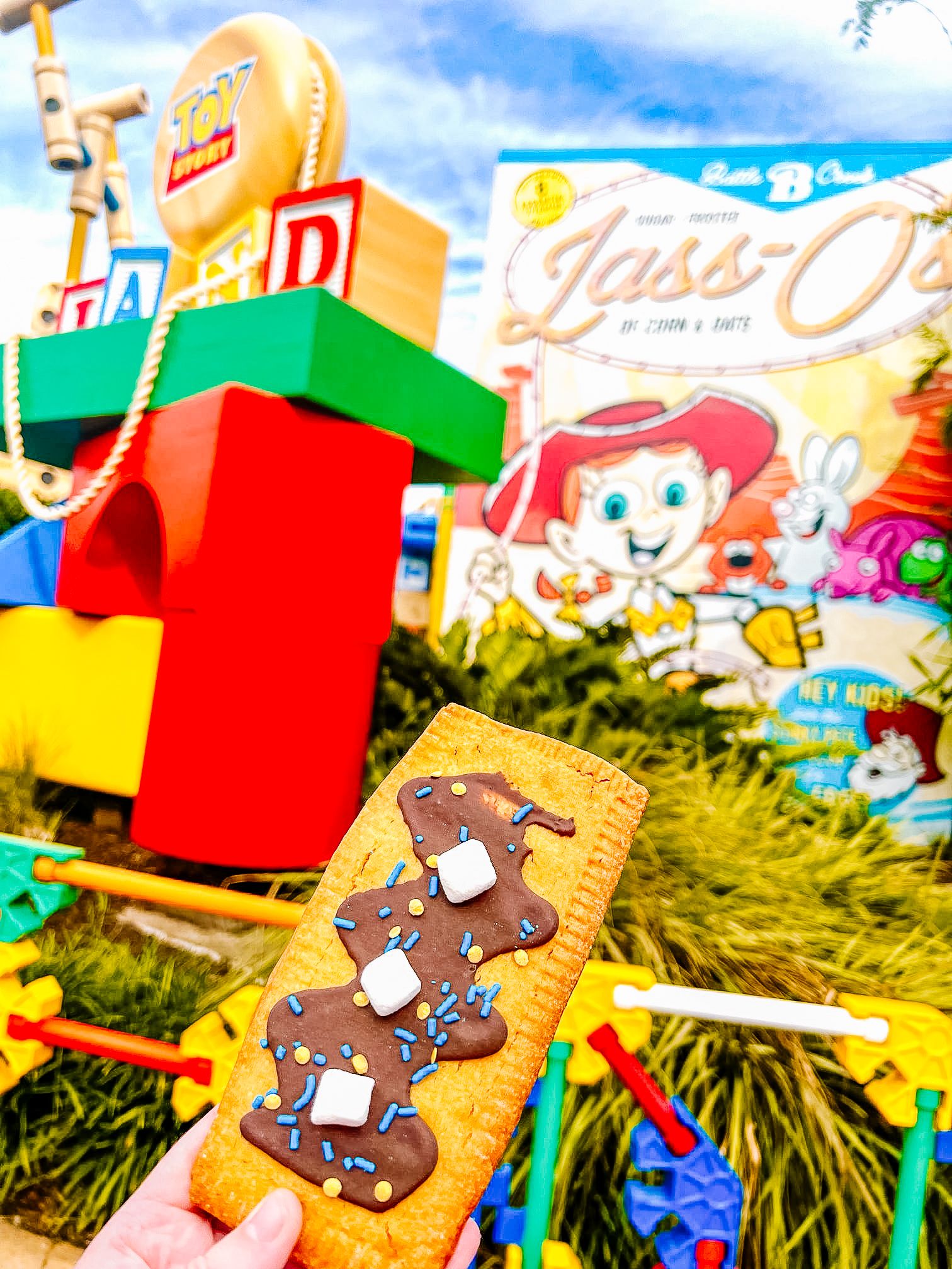 Colorful LEGO-themed dessert held in front of Toy Story Land decorations at Disney World.