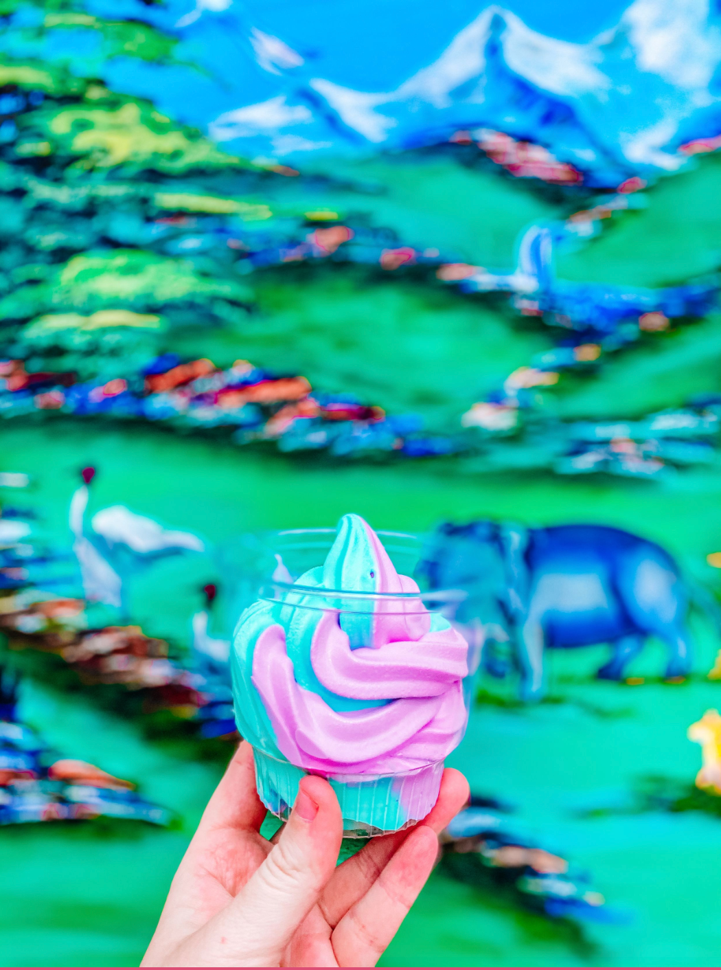 Swirled blue and pink unicorn-themed ice cream against a blurred mountain landscape background.