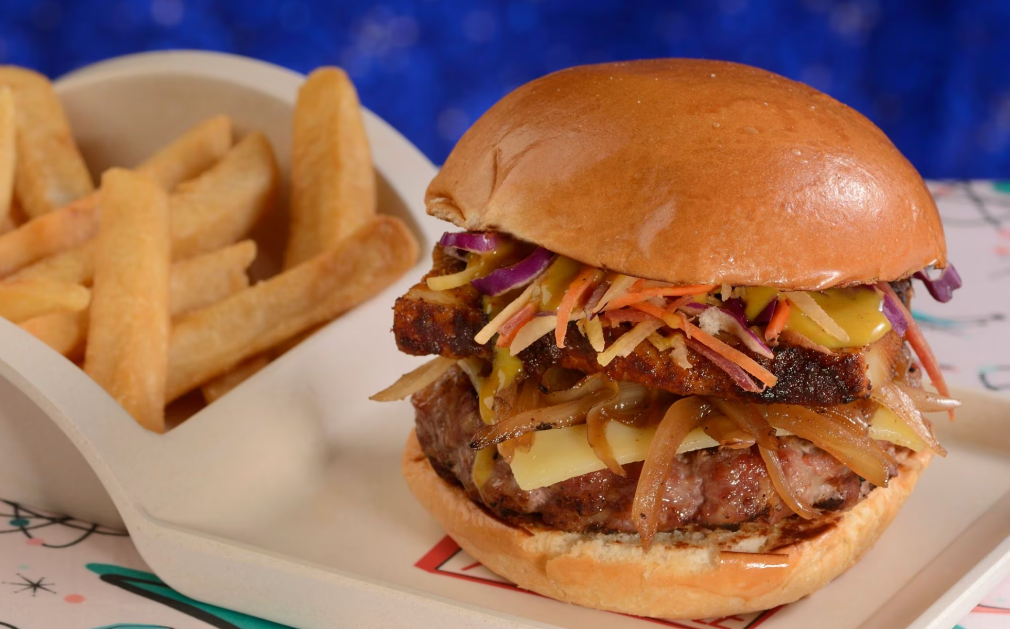 Close-up of a gourmet burger with melted cheese and french fries on a diner placemat.