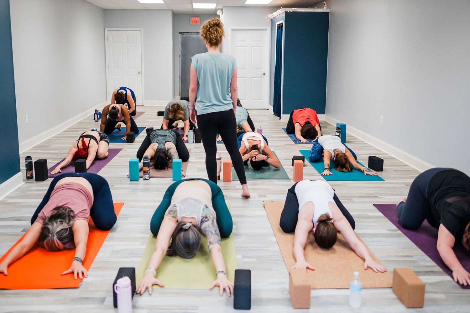 Group of people practicing yoga poses on colorful mats in a bright studio space during a fitness class.