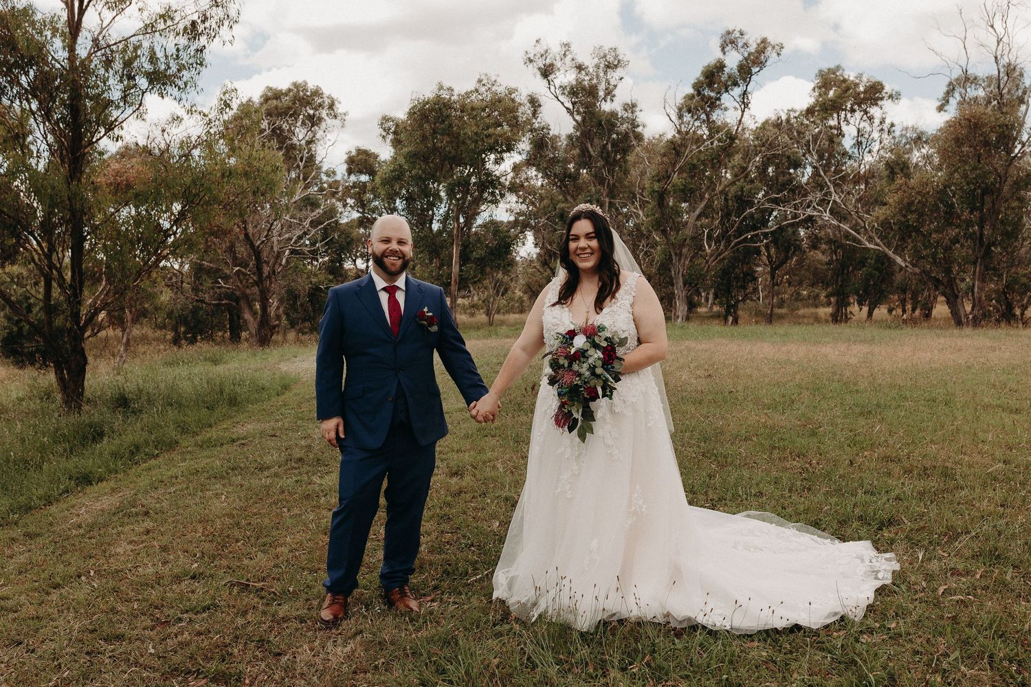 A rustic outdoor wedding photograph with a couple holding hands in an Australian bush setting.