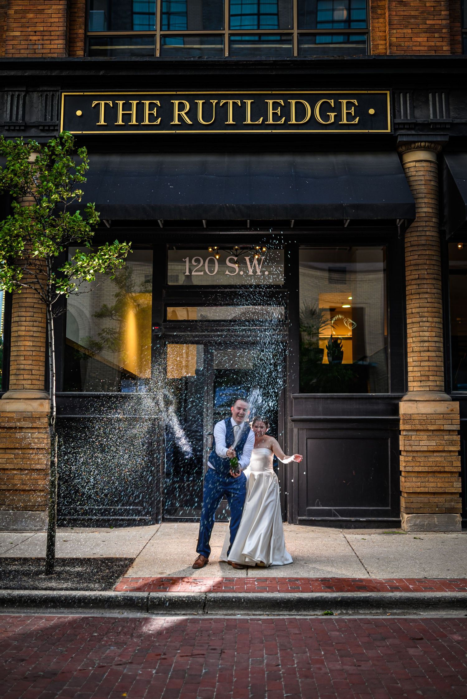 A wedding couple getting sprayed with water in front of The Rutledge building entrance.