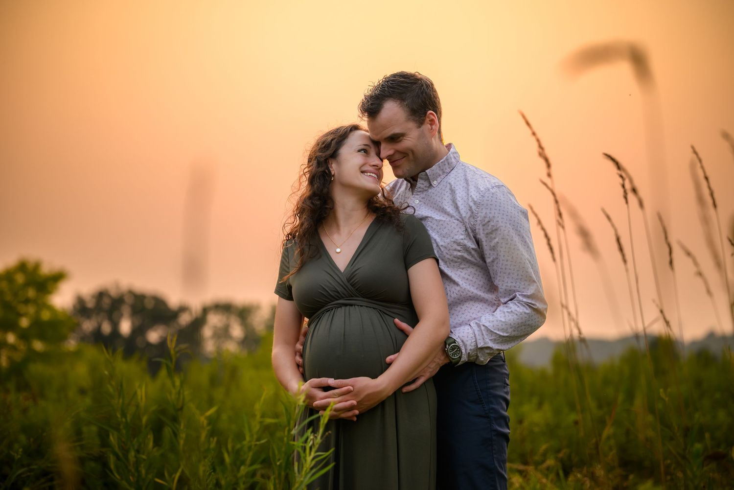 A couple embraces in a golden field during sunset while sharing an intimate moment together.