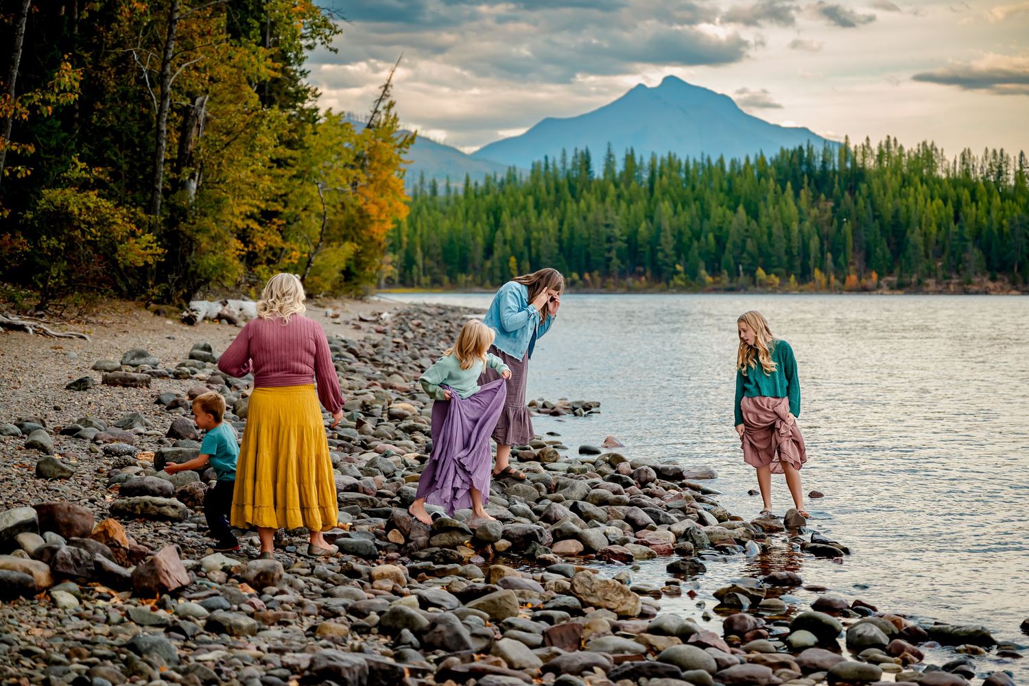 Group enjoying a scenic mountain lake view while standing on a rocky shoreline during golden hour.