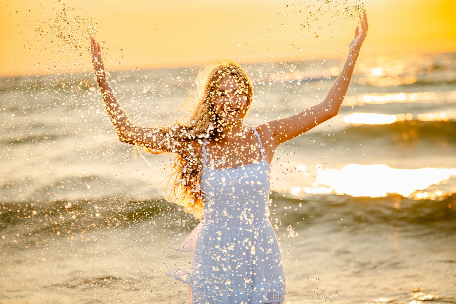 Splashing waves crash against the beach during golden sunset creating a dreamy summer scene.
