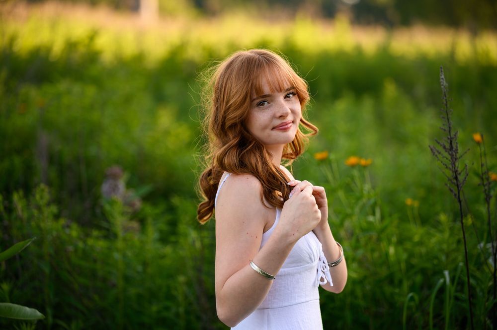 A young woman in a white dress poses in a sunny meadow filled with wildflowers at golden hour at The Highlands in Grand Rapids