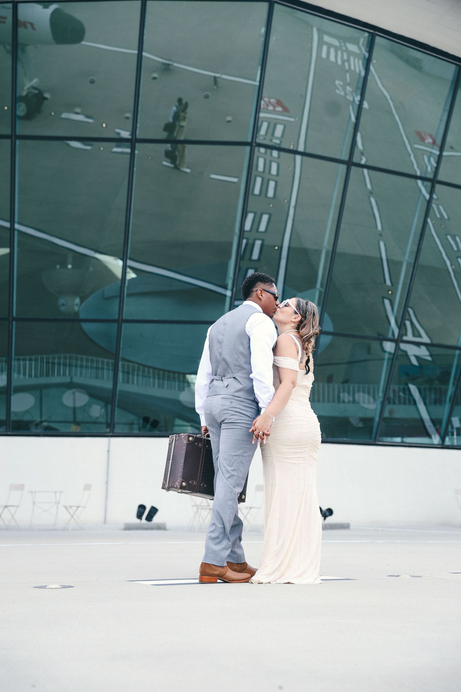 Couple in formal wear embracing in front of modern glass building architecture.