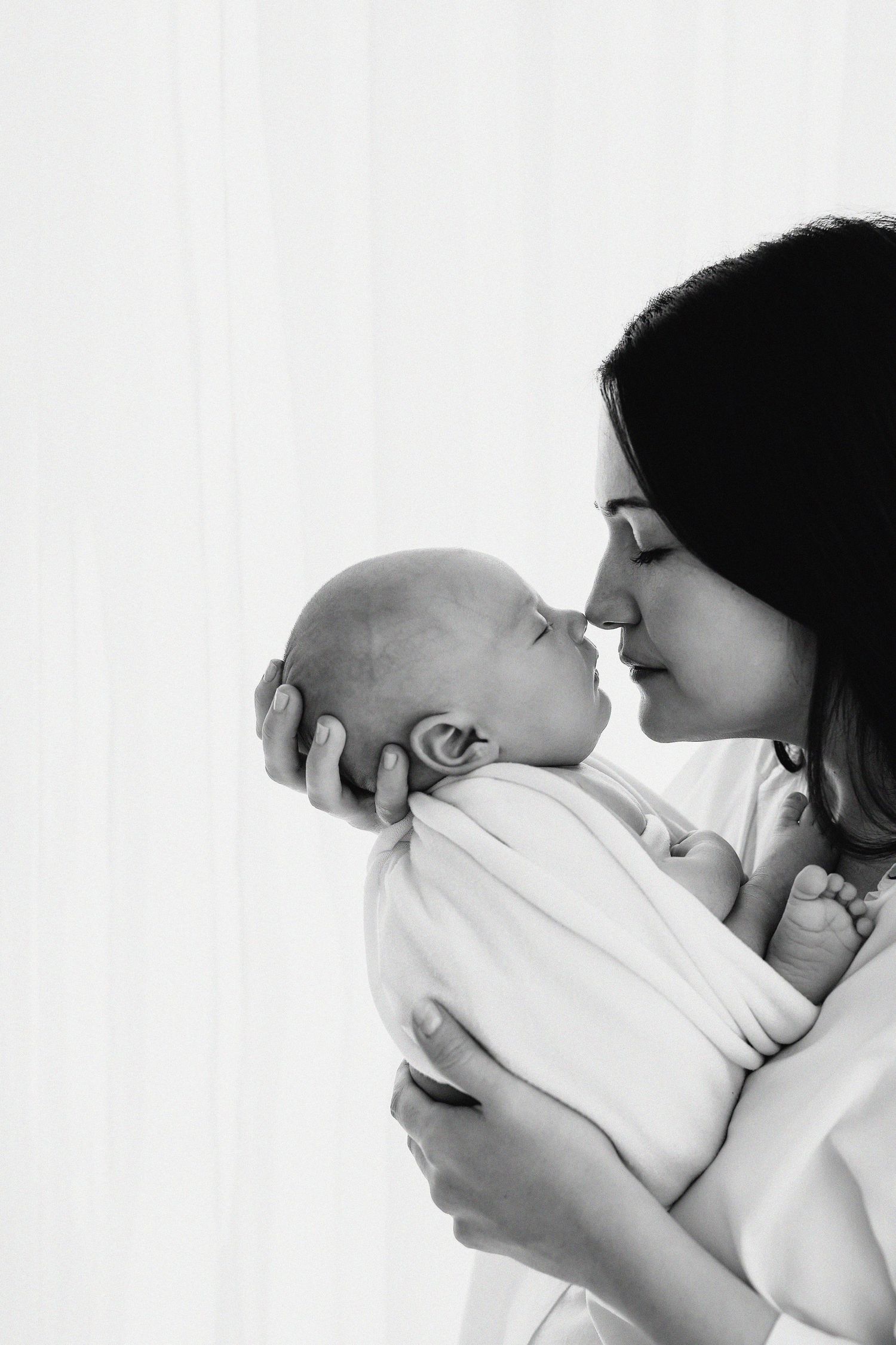 A tender moment captured in black and white as parent and newborn share an intimate nose-to-nose connection.