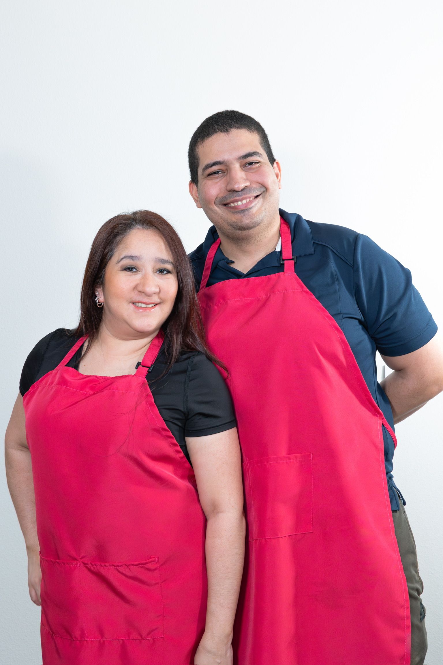 Two people wearing bright red aprons pose together against white background.