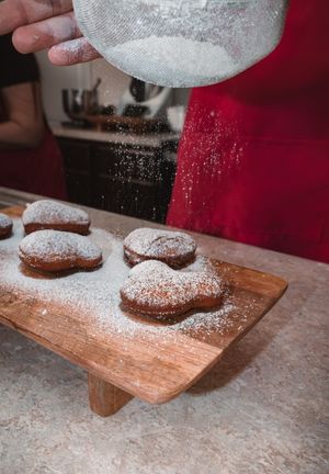Powdered sugar being sifted over chocolate cookies on a wooden cutting board.
