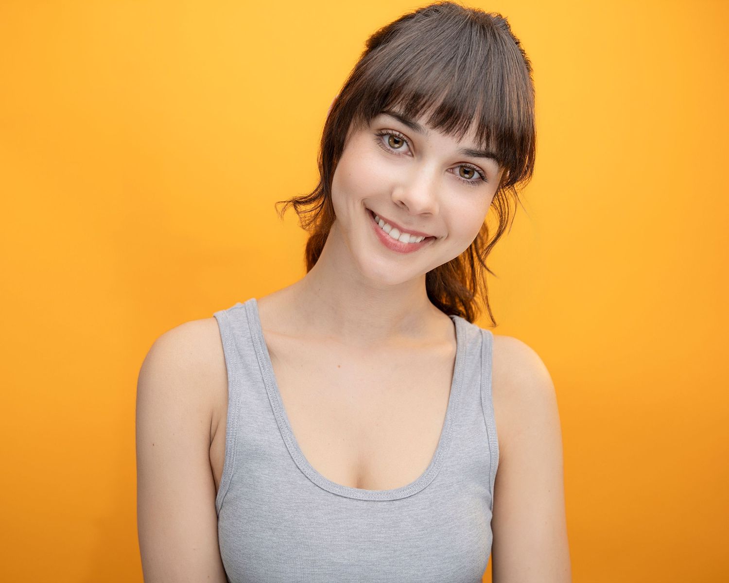 A portrait against white background features a person in a sleeveless white top with blonde hair styled straight back.