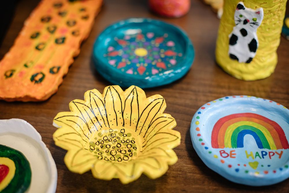 Colorful clay decorations featuring rainbow designs, sunflowers, and positive messages displayed on a wooden surface.