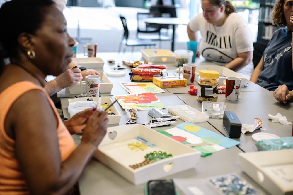 Arts and crafts workshop participants work on colorful paper projects at tables during creative group activity.