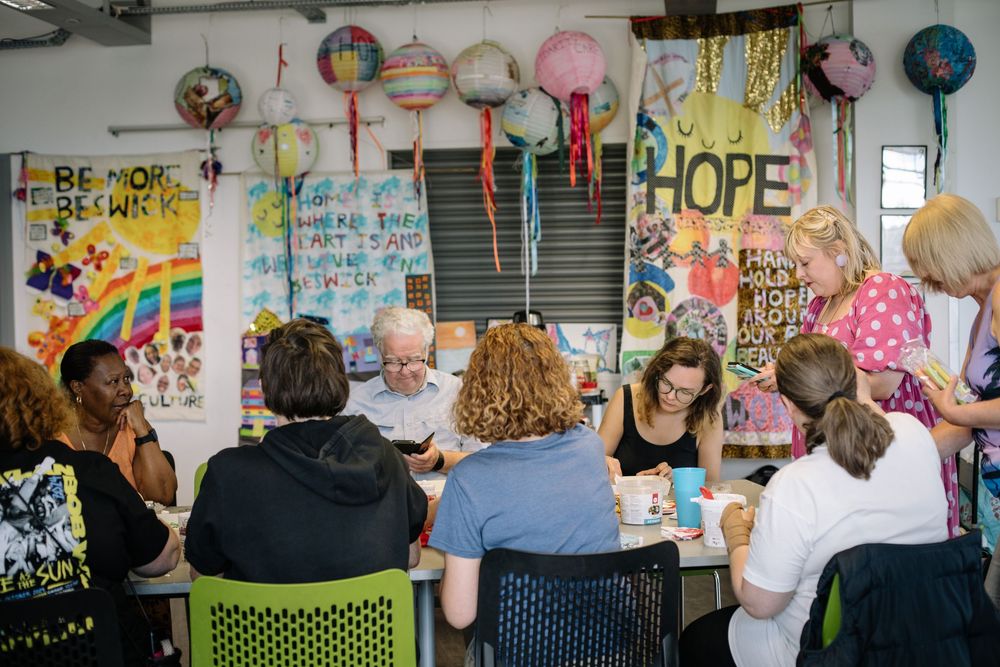 A group of workshop participants gather around tables working on colorful art and crafting projects together.