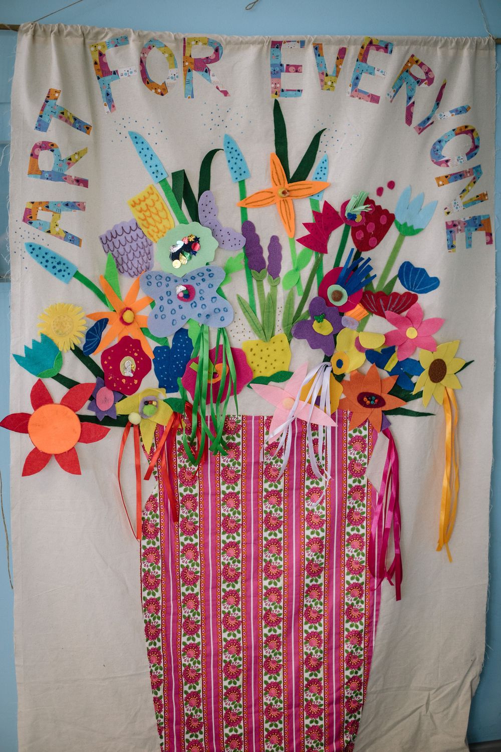A colorful arts and crafts display shows paper flowers and decorative elements on a pink striped curtain background.