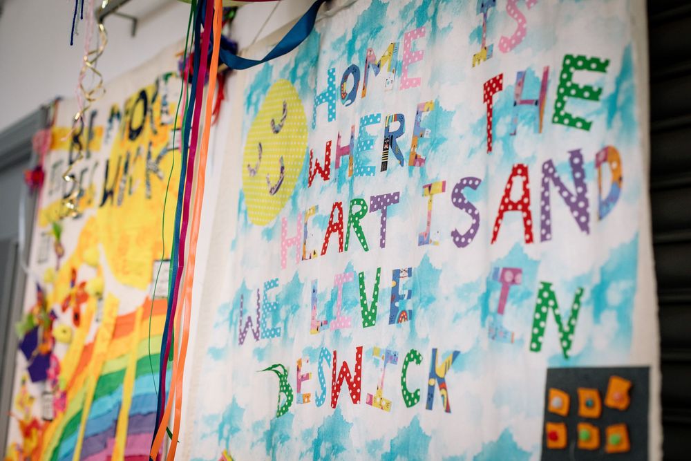 Colorful student artwork displaying handwritten text and mixed media designs hangs on a classroom wall.