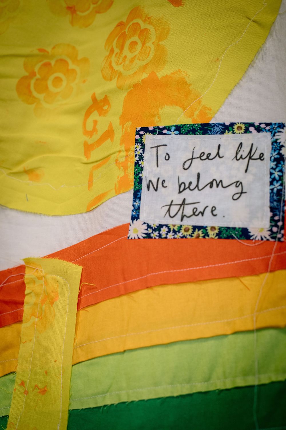 Abstract art featuring yellow, orange, and green stripes with handwritten text fragments visible in the upper portion of the image.
