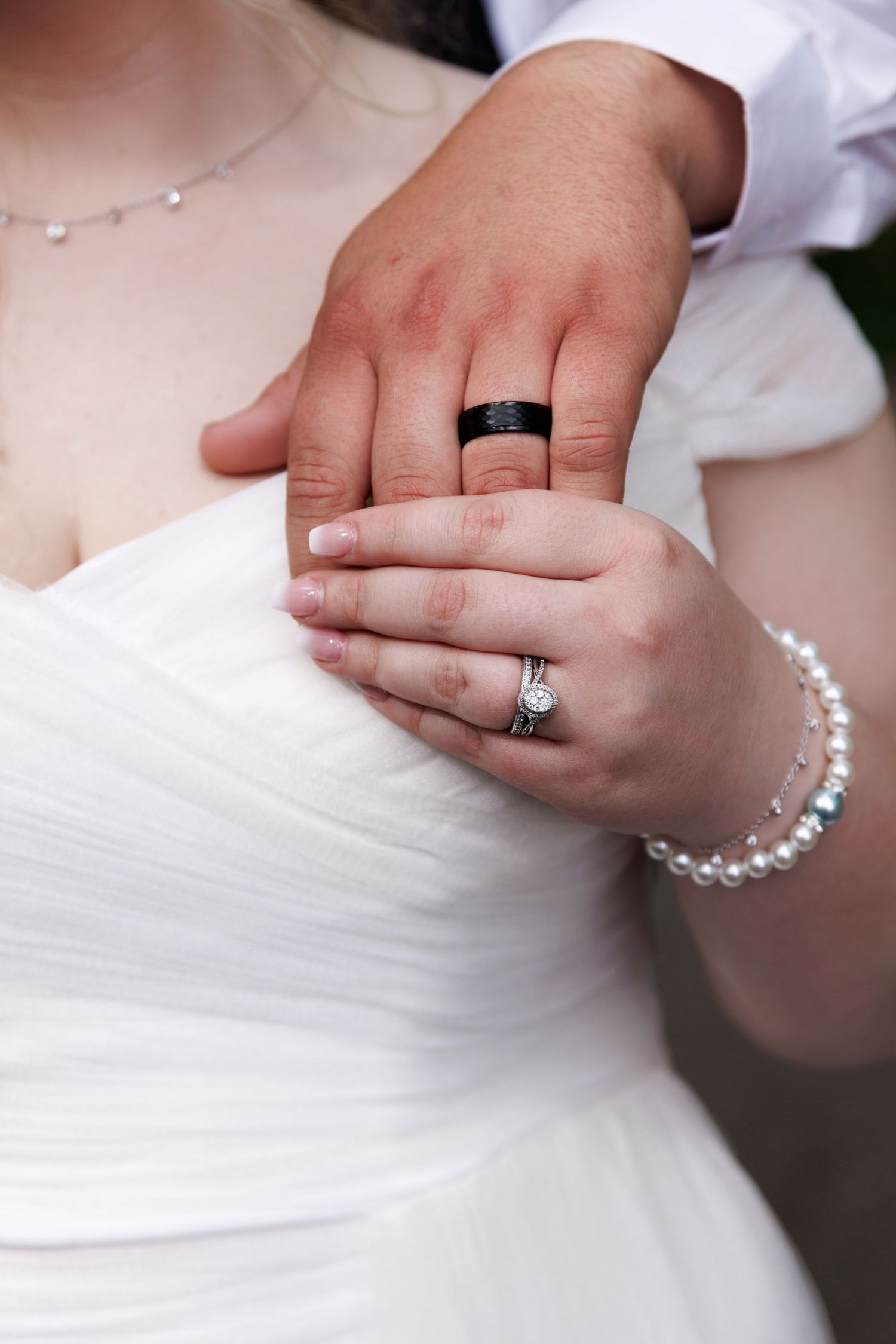 Close-up of bride and groom hands showing wedding rings, bride wearing diamond ring and pearl bracelet.