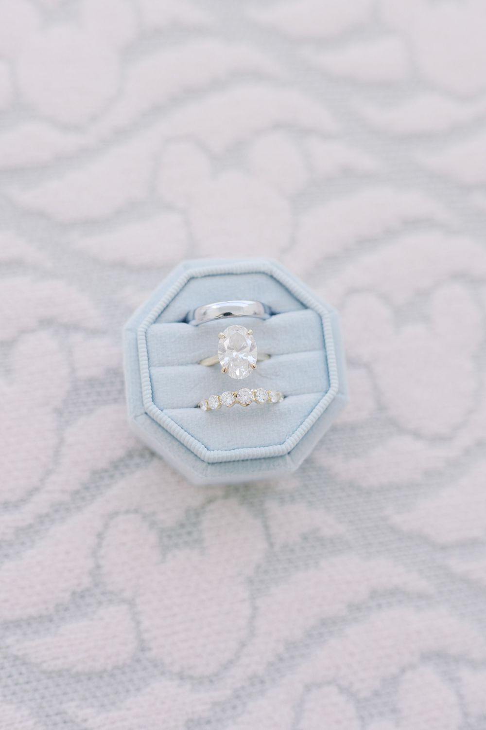 Oval diamond engagement ring and diamond wedding band displayed in a light blue octagonal velvet ring box.
