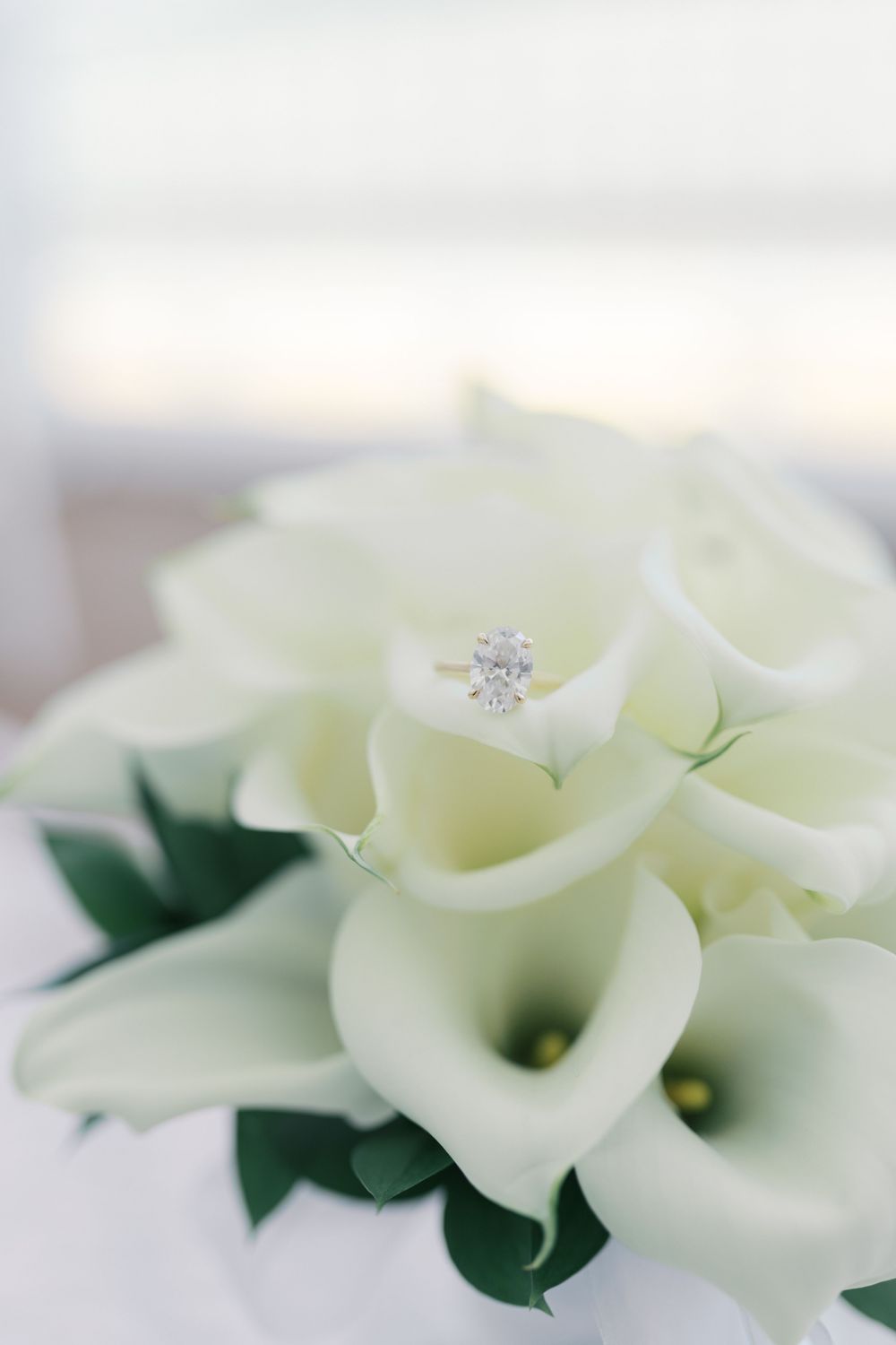 Diamond engagement ring nestled in a white calla lily bridal bouquet close-up detail shot.