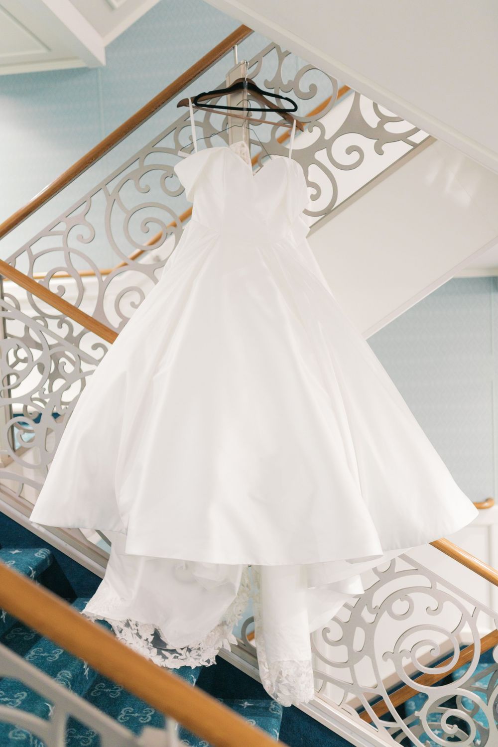 Elegant white ball gown wedding dress hanging on a hanger over a decorative staircase railing.