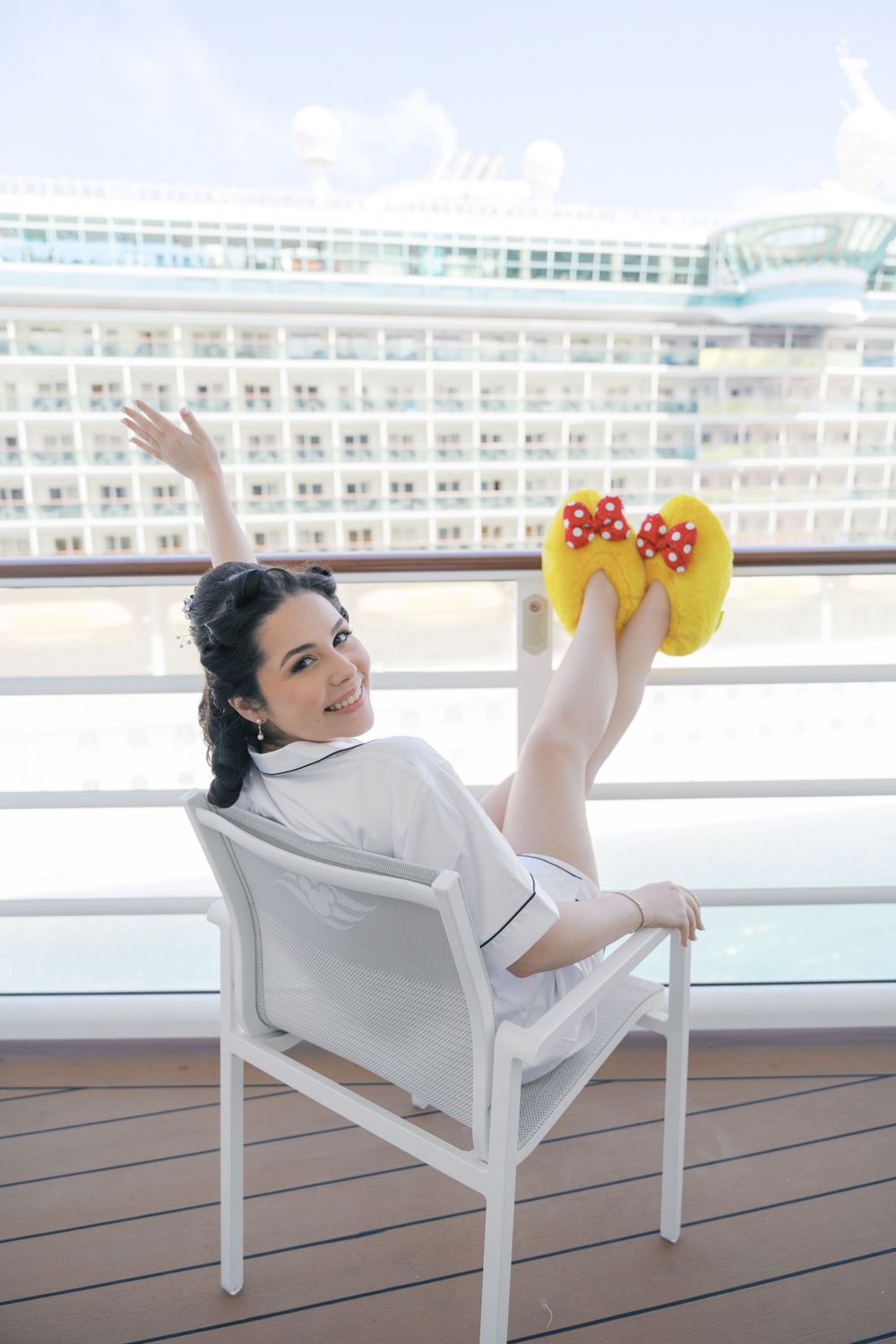 Happy bride in white robe wearing yellow Minnie Mouse slippers on a cruise ship balcony.