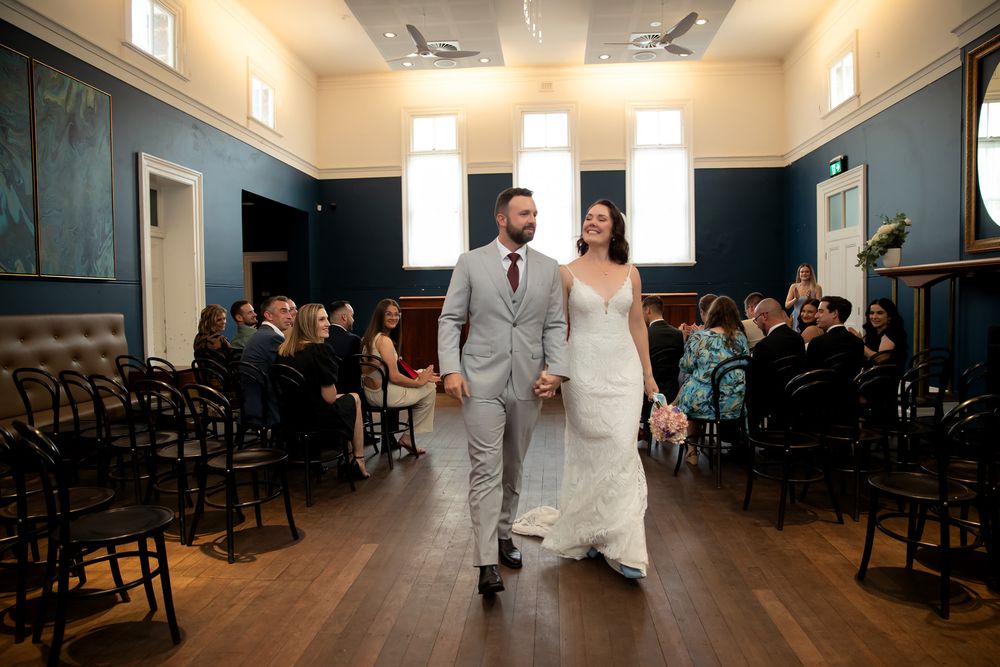 Bride and groom walk hand-in-hand down the aisle in an elegant blue-walled venue after their wedding ceremony.