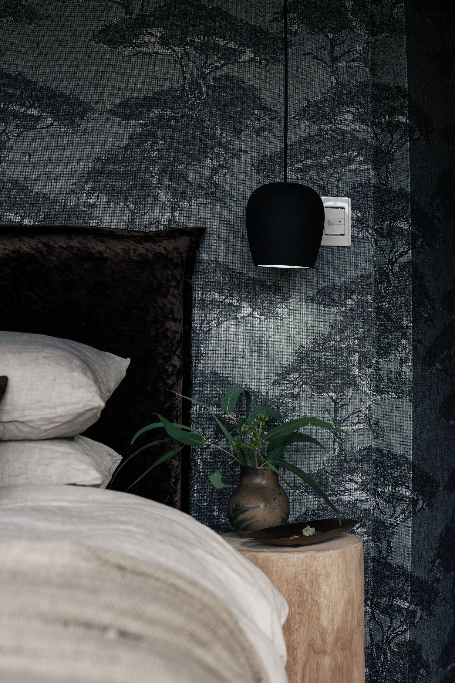 Dark moody bedroom with forest landscape wallpaper, black pendant light, and linen bedding.

The Empress