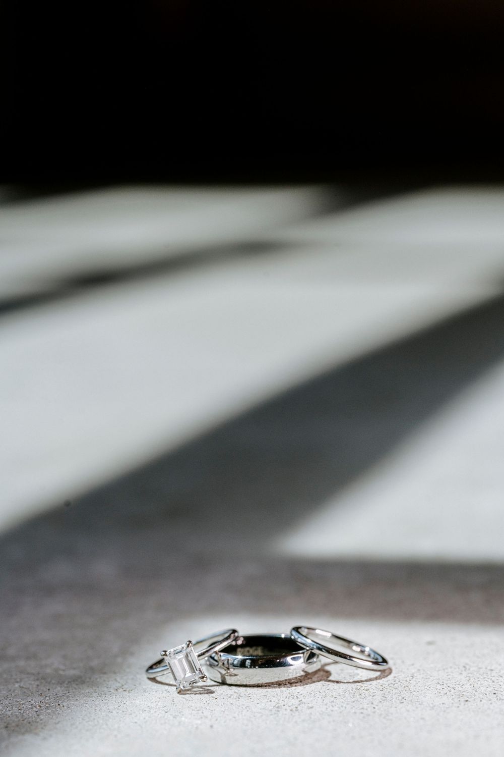 Three wedding rings, including a diamond engagement ring and two bands, arranged on a light gray surface with shadows.