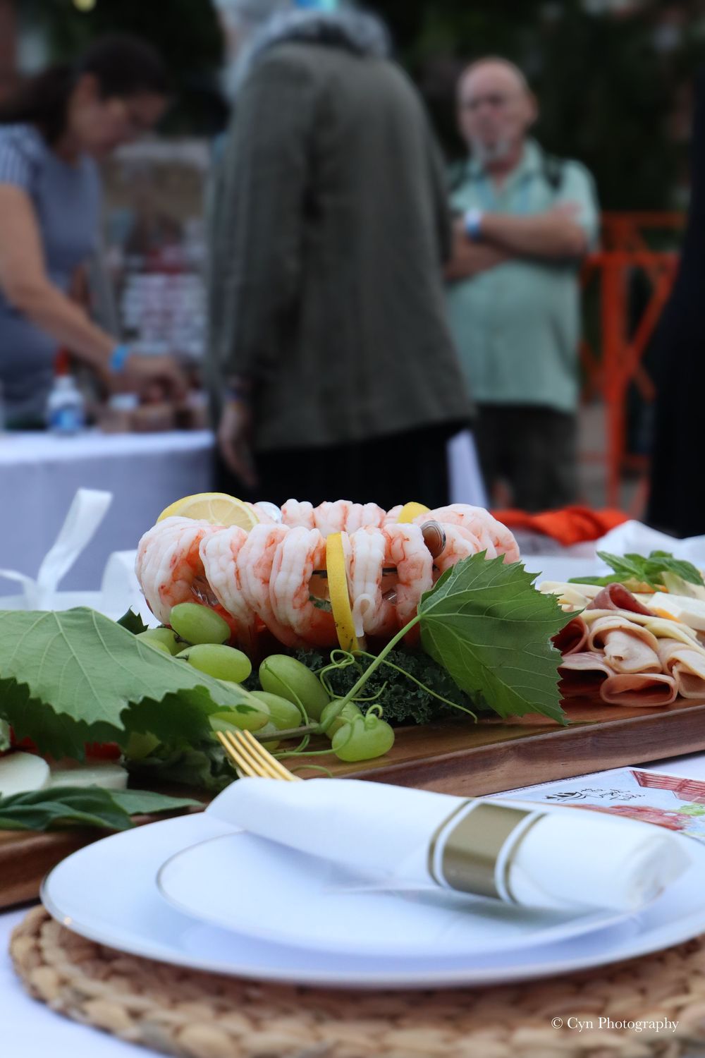 Elegant outdoor shrimp cocktail platter with grapes and lemon on wooden board, set at a formal dinner party event.