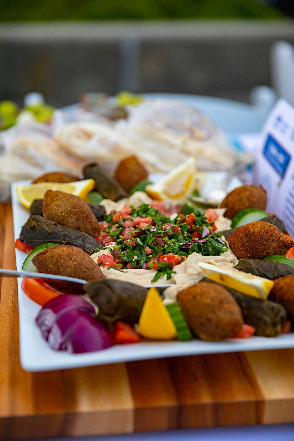 A vibrant Middle Eastern mezze platter with falafel, tabbouleh, hummus, stuffed grape leaves, and fresh vegetables on a white plate.