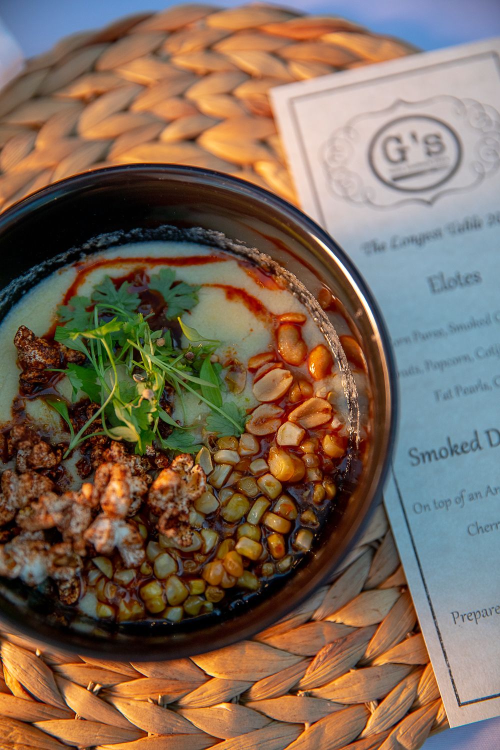 Bowl of elotes corn soup garnished with microgreens, peanuts, and chili oil at G's restaurant event.