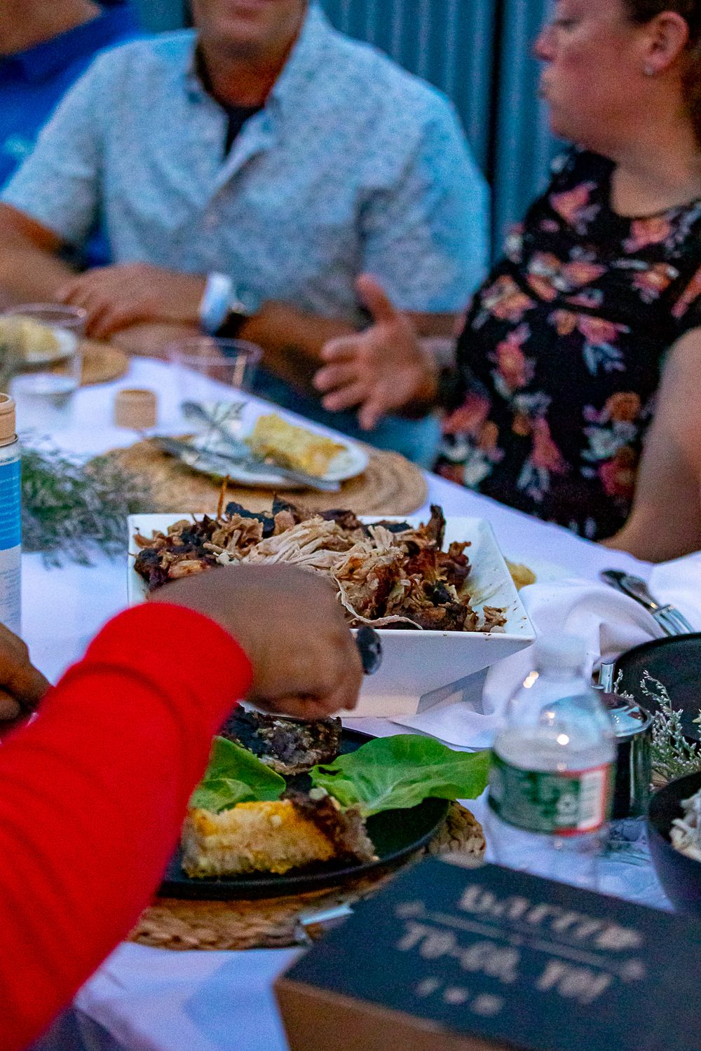 People gathered around a table enjoying a meal with pulled pork and fresh greens served on a platter.