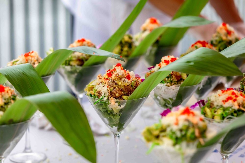 Elegant martini glasses filled with colorful gourmet appetizers garnished with red caviar and fresh green leaves at a catered event.