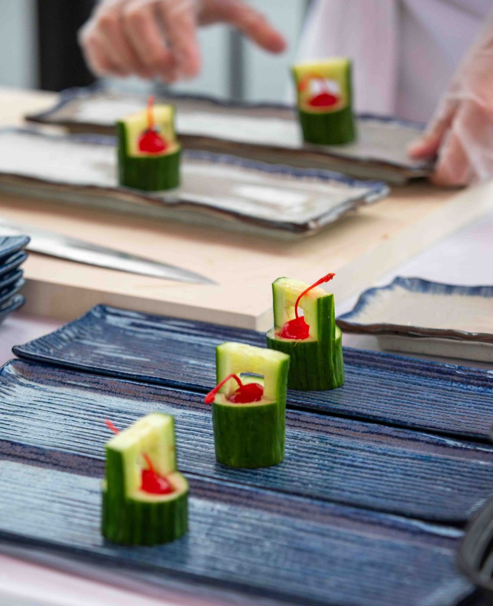 Chef plating cucumber roll appetizers filled with red pepper garnish on blue ceramic rectangular plates.