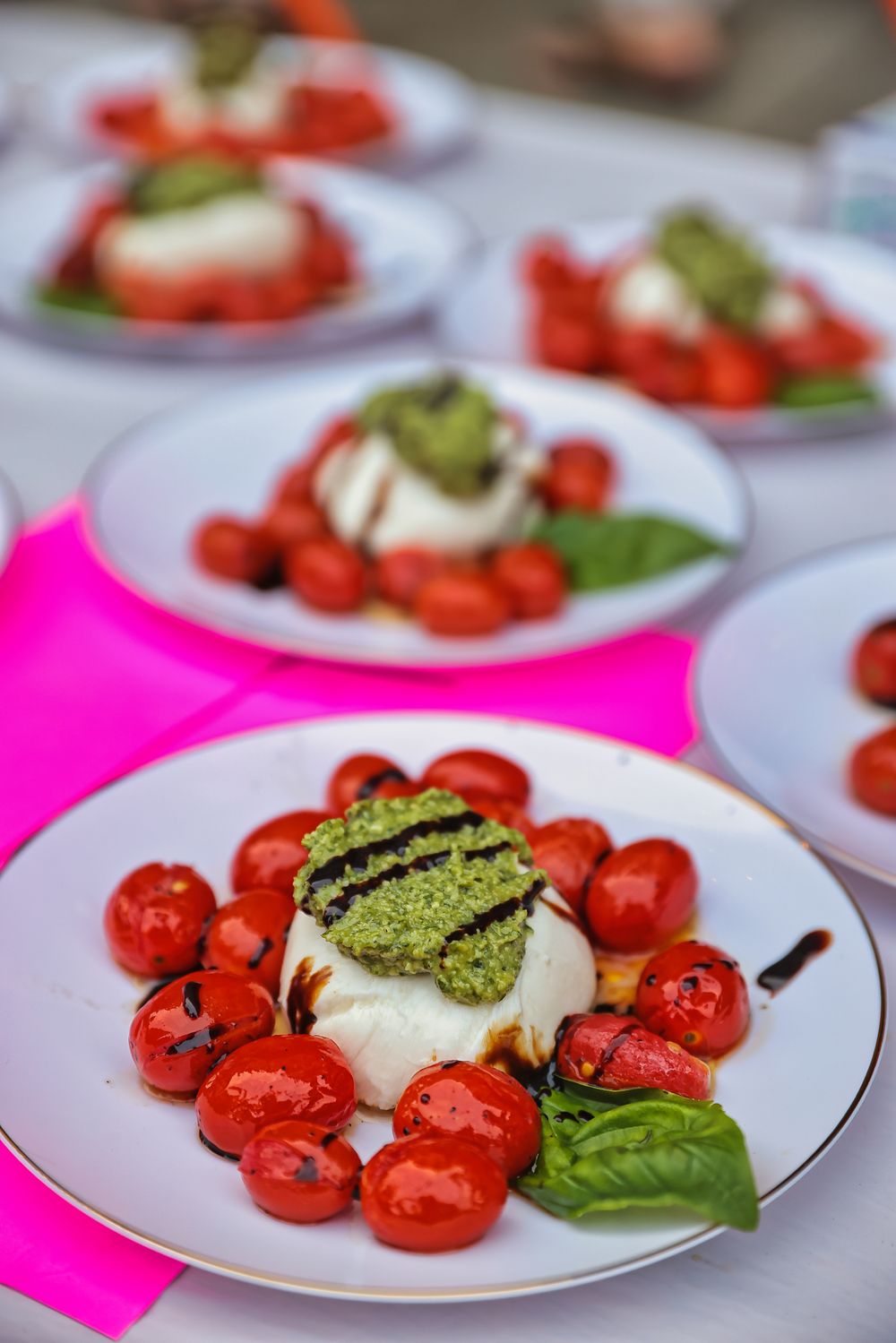 Caprese salad plates featuring fresh mozzarella, roasted cherry tomatoes, pesto, and basil at an outdoor catered event.