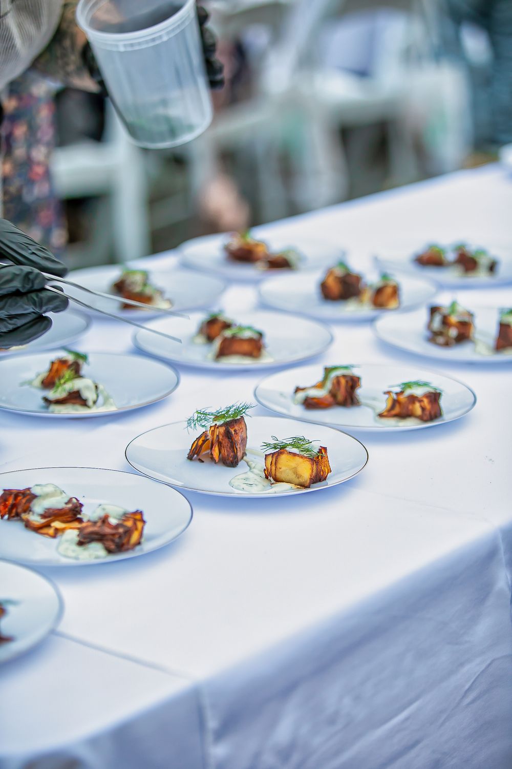 Catered event with rows of plated roasted meat appetizers with green herb sauce on white round plates.